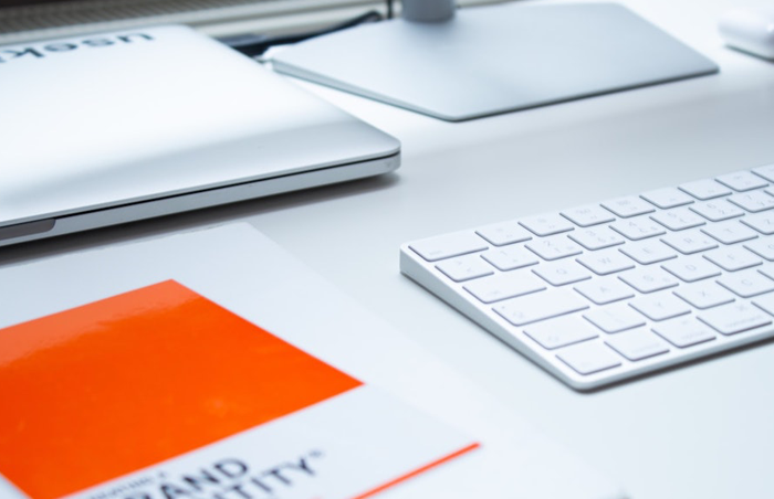 A brand identity guidelines booklet on a desk beside a laptop and keyboard