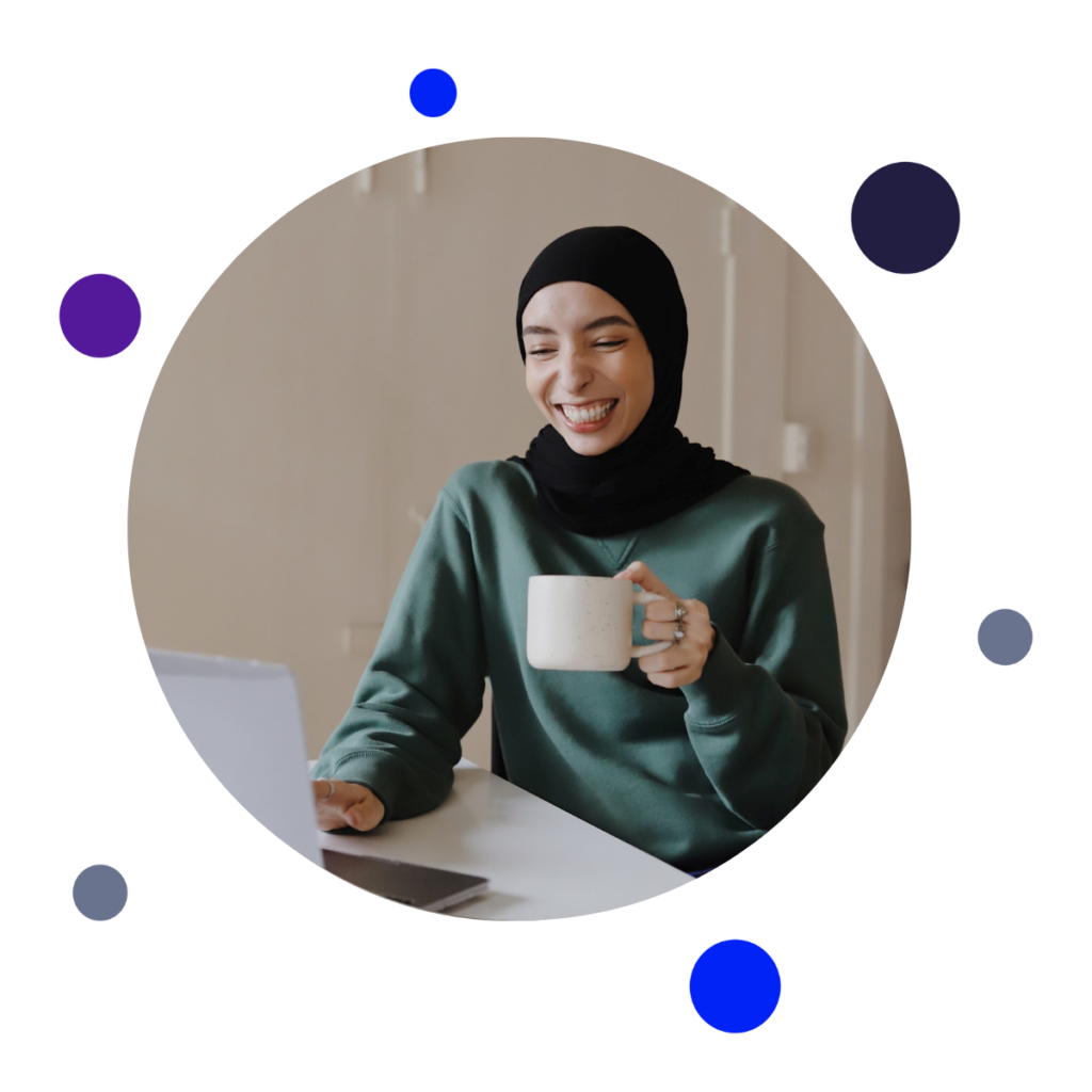 Woman smiling at laptop with a coffee mug in her hand