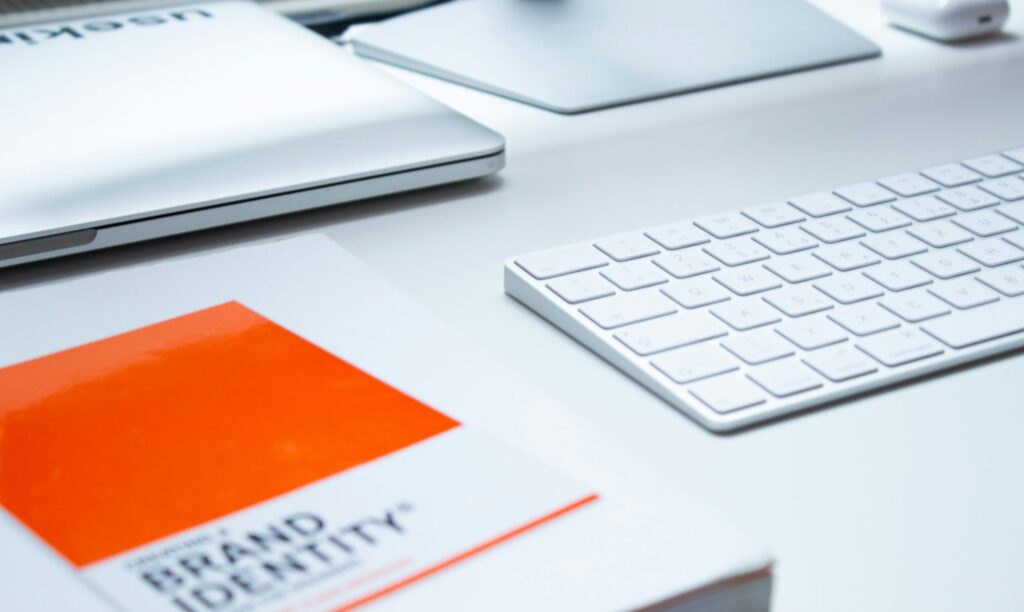 A desk, mostly in white, with a brand identity book next to the keyboard.